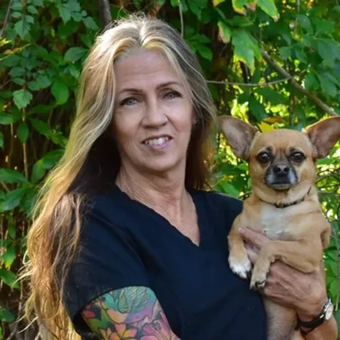 Woman with tattooed arm holding a small chihuahua outdoors